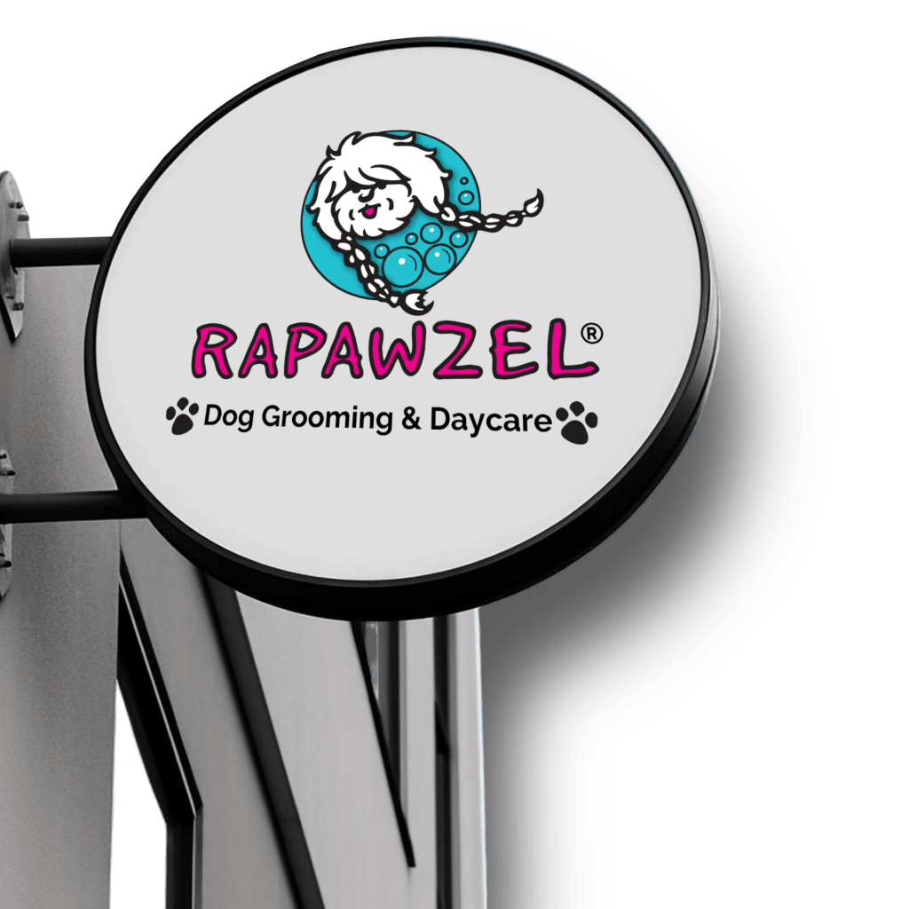 Round sign for "Rapawzel Dog Grooming & Daycare" with a cartoon dog, teal bubbles, and paw prints, mounted on a building exterior—perfect for showcasing your trusted pet groomer and pet daycare services.